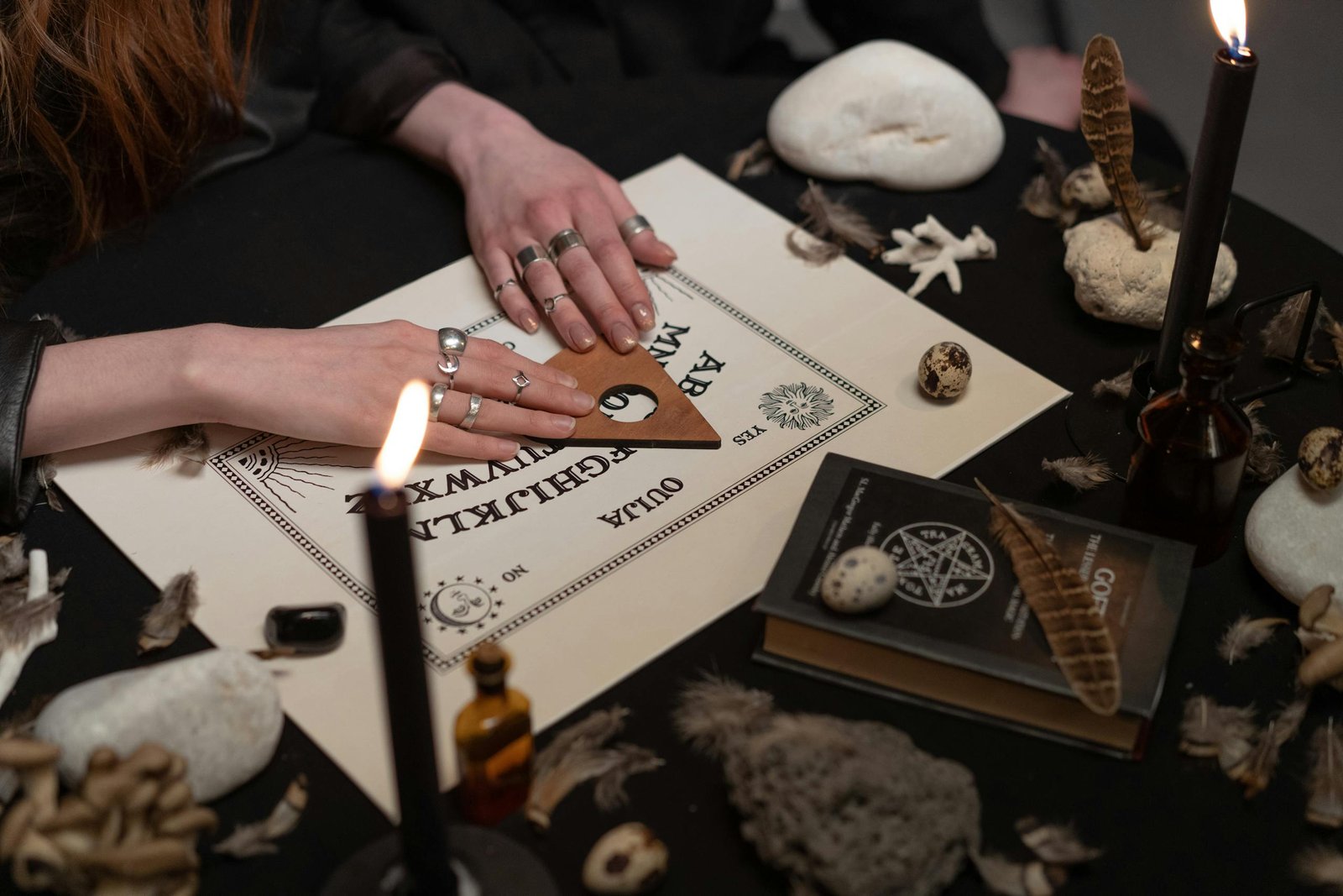 Hands of Women on a Ouija Board Near Burning Candles