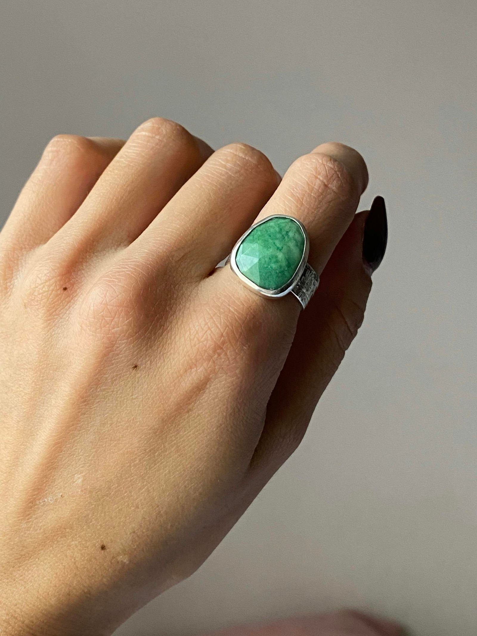 A hand holding a green stone ring