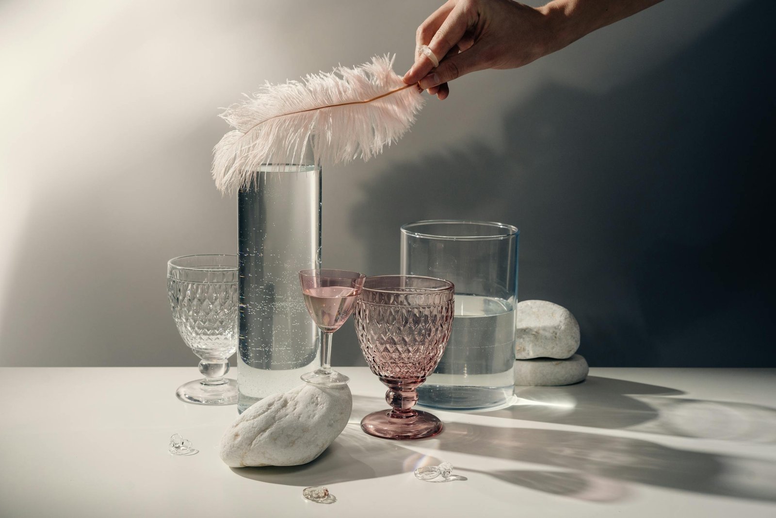 Person Holding White Feather Beside Clear Drinking Glass