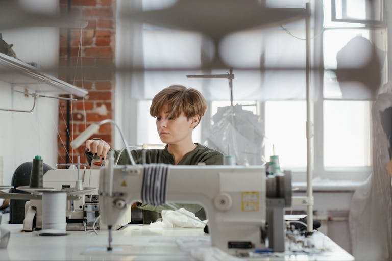 A woman intensely focused on sewing in a modern, well-lit workshop with sewing machines.